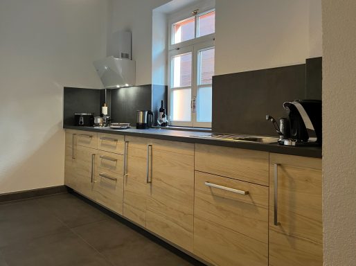 Küche mit Küchenzeile, Herd, Spülbecken, Kühlschrank, Gefrierfach, Kaffeemaschine, Toaster, Wasserkocher, Geschirr und Besteck 
