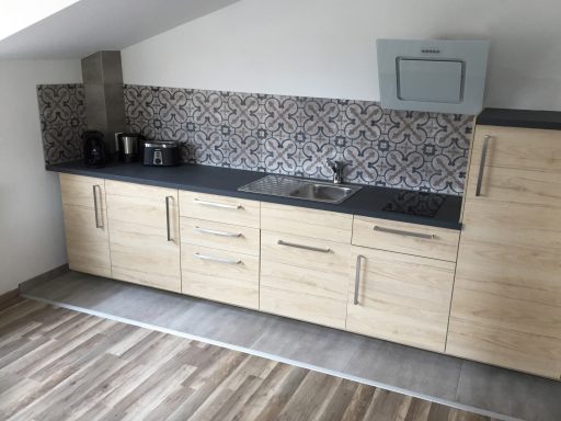 Küche mit Küchenzeile, Herd, Spülbecken, Kühlschrank, Gefrierfach, Kaffeemaschine, Toaster, Wasserkocher, Geschirr und Besteck 
